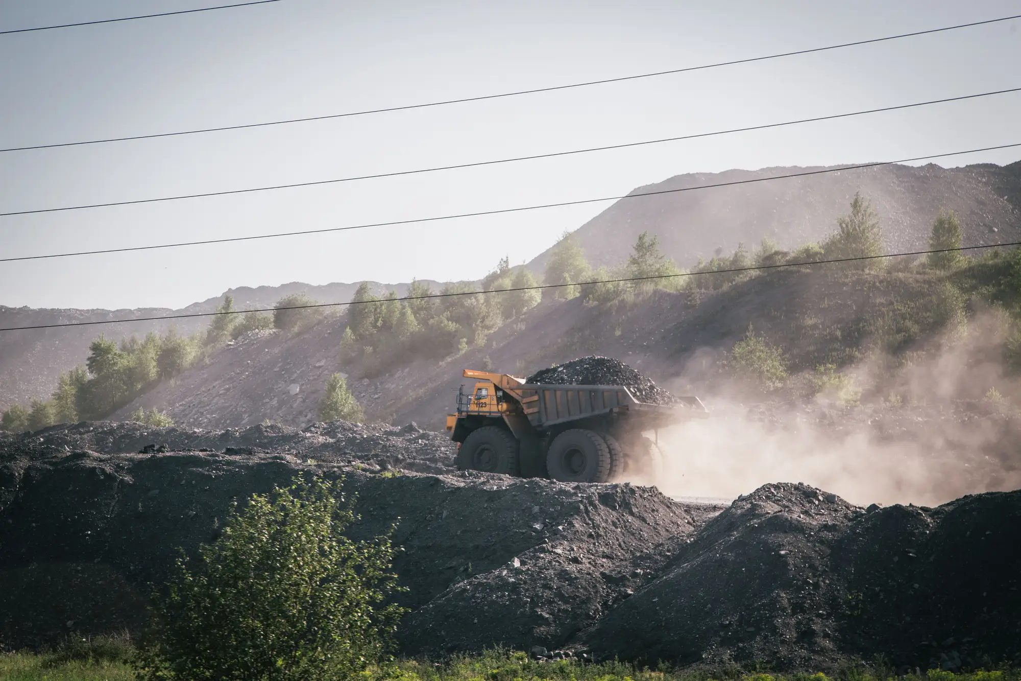 A loaded haul truck raising dust on a mine road below a spoil heap
